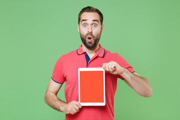 Wall Mural - Shocked young bearded man guy in casual red pink t-shirt posing isolated on green wall background studio. People lifestyle concept. Mock up copy space. Hold tablet pc computer with blank empty screen.