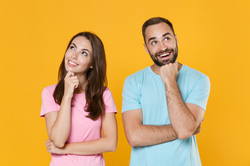 Pensive young couple two friends guy girl in blue pink t-shirts isolated on yellow background studio portrait. People lifestyle concept. Mock up copy space. Put hands prop up on chins, looking up.