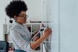 © Svitlana - Distance education. Close up of a young afro american female teacher writing on a whiteboard while teaching English language online, working from home