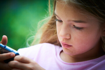 Wall Mural - Child girl playing on smartphone playing games outdoors during summer day