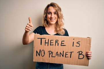 Young blonde activist woman asking for environment holding banner with planet message happy with big smile doing ok sign, thumb up with fingers, excellent sign