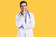 Young hispanic man wearing doctor uniform and stethoscope looking confident at the camera smiling with crossed arms and hand raised on chin. thinking positive.