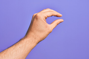 Hand of caucasian young man showing fingers over isolated purple background picking and taking invisible thing, holding object with fingers showing space