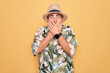 Young handsome man with blue eyes on vacation wearing summer florar shirt and hat shocked covering mouth with hands for mistake. Secret concept.