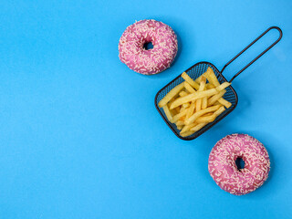 Two American pink cream donuts and fried potatoes in an iron basket on the right, with space for text on the left, against a light blue background. Close-up top view.