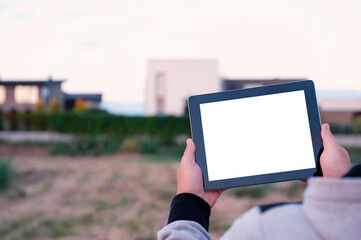 Mock up of a tablet with white screen in hands, against the background of modern houses.