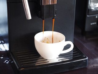 Pouring coffee pouring from maker machine into white cups