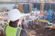 Leinwandbild Motiv construction worker or civil engineer or architect or foreman with hard hat and safety vest at major construction site with crane and digger supervising with walkie talkie