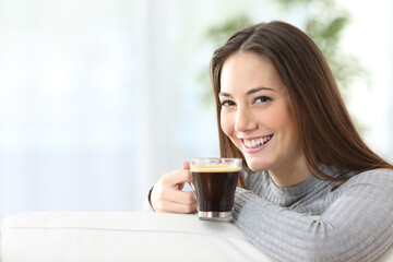 Wall Mural - Happy woman with coffee cup looking at camera at home