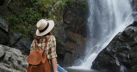 Canvas Print - Woman goes hiking and looks at the waterfall in forest