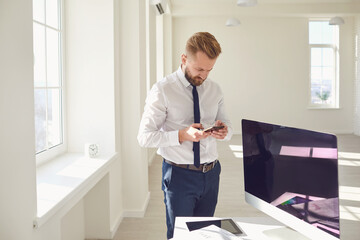 Wall Mural - A bearded businessman uses a mobile reads sms text while standing in the workplace at the office.