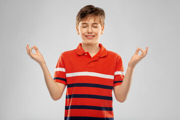 childhood, fashion and people concept - happy smiling boy in red polo t-shirt meditating over grey background