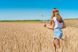 © KseniaJoyg - A charming little girl a child in denim shorts walks through a wheat field and collects spikelets