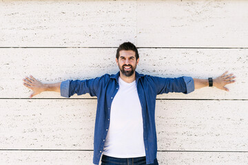 Bearded male leaning on wall with Stretched arms while looking camera with a smile