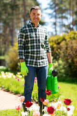 Wall Mural - gardening and people concept - happy smiling middle-aged man with watering can and flowers at garden