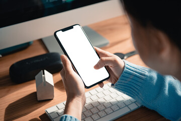 Hand touching mobile smartphone with blank white screen on the desk in the office, copy space.