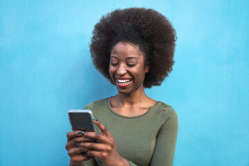Wall Mural - Young Afro woman using mobile smartphone - Happy African girl having fun with new trends technology apps - Youth millennial generation z and social influencer concept - Blue background