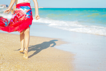 A girl in a pareo walks along the sand along the seashore. Family travel concept.