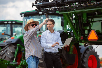 Professional farmer with a modern combine at field in sunlight at work. Confident, bright summer colors. Agriculture, exhibition, machinery, plant production. Senior man near his tractor with investor