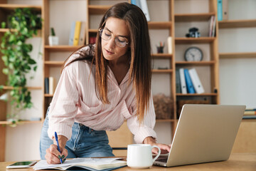 Wall Mural - Image of businesswoman writing down notes while working with laptop