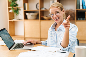 Poster - Image of woman pointing finger at camera while working with laptop