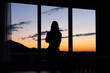 © Vasya - Silhouette of a woman standing in front of a window with sunset in the background