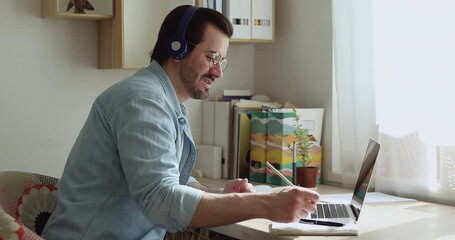 Wall Mural - Man talks through wireless headphones with colleague or online tutor while working on project or study language, look at laptop screen enjoy distant communication by video call conference app concept