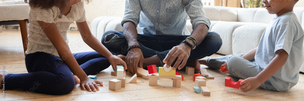 Close up wide banner panorama view of playful african American father with small kids sit on floor play with building bricks, biracial dad with little children construct with wooden blocks at home - obrazy, fototapety, plakaty 