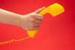 © Nikolay - Yellow handset on a red background in woman hand.