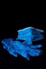 Sticker - Vertical shot of a blue protective face mask and plastic gloves on a black background