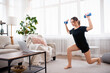 © Admiral - Online workout at home. Attractive young woman doing exercises with dumbbells in living room. Sport, entertainment and education on the Internet.
