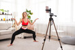 © Admiral - Fitness online coaching concept, sport in modern technologies. Young female trainer broadcasts stretching workout online using smartphone
