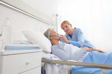 nurse puts oxygen mask on elderly woman patient lying in the hospital room bed