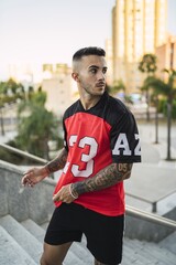 Wall Mural - European hip male in a sporty outfit with red and black shorts and shirt, tattoos, and metal chain