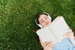 © LIGHTFIELD STUDIOS - top view of attractive woman in wireless headphones lying on grass and reading book