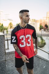 Wall Mural - European hip male in a sporty outfit with red and black shorts and shirt, tattoos, and metal chain