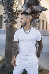 Wall Mural - Vertical shot of a young European tattooed hip male in white shorts and shirt and a metal chain