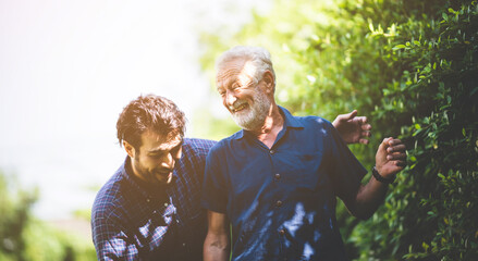 An adult hipster son and senior father talking at home, morning nature scene in the home garden outdoor