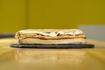 Poster - Closeup shot of a sandwich with mayonnaise on a black round board on a wooden table