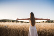 Young woman on her back opens her arms in the field feeling free. Blonde girl with long hair enjoys the summer sun