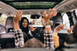 © Maskot - Cheerful family raising hands while enjoying road trip in electric car