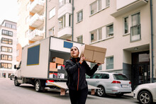 Young delivery woman carrying box on street