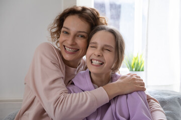 Head shot portrait overjoyed mother and happy teenage daughter hugging, looking at camera, excited mum and teenager girl with healthy toothy smile cuddling, making video call, shooting vlog