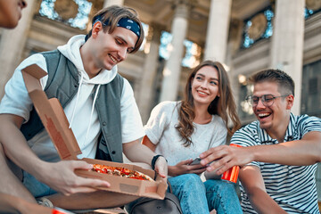 Wall Mural - A group of students sit on the steps outside the campus and eat pizza and soda. A group of friends are relaxing and chatting.