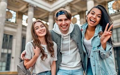 Wall Mural - A group of students on the street near the university campus. Three friends are happy to meet, hug and laugh.