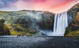 Impressively beautiful nature of Iceland during sunset. Skogafoss waterfall is one famous natural landmark and travel destination place of Iceland. Tourists ride horses near famouse waterfall.