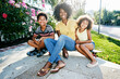 © Tetra Images - Smiling mother and children sitting on skateboard on sidewalk