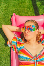 Portrait Of Woman Wearing Glasses With Colourful Pom Poms Covering Her Eyes Relaxing On Pink Airbed