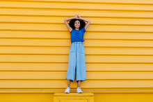 Smiling Woman Standing On Platform In Front Of Yellow Wall