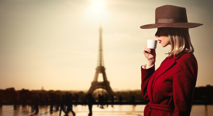  girl in red coat drink a coffee wit hEiffel tower on backgorund